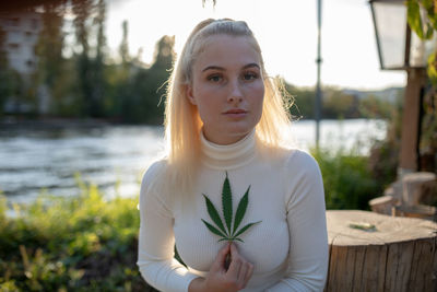 Portrait of woman holding marijuana against sky