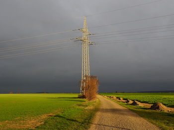 Transmission tower on field against sky