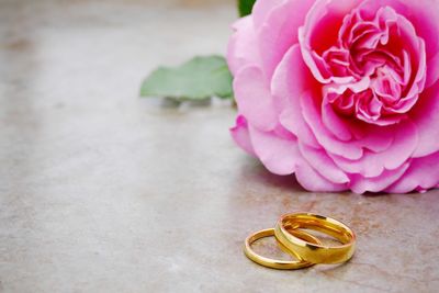 Close-up of wedding rings and rose flower on table