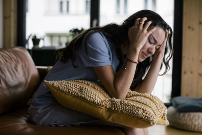 Frustrated young woman with head in hands sitting on sofa at home