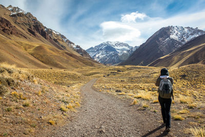 Rear view of backpacker walking on field by mountains against sky