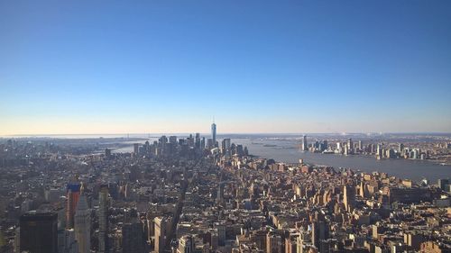 Cityscape by river against clear blue sky