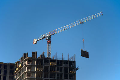 Low angle view of crane by building against clear blue sky