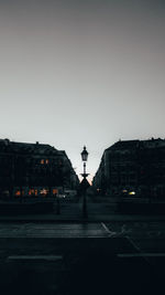 Street by silhouette buildings against clear sky