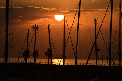 Silhouette sailboats in sea against orange sky