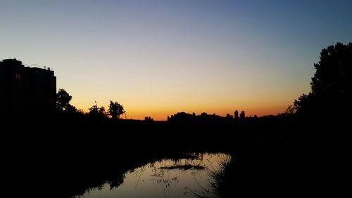 Silhouette trees by lake against sky during sunset