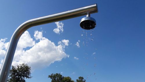 Low angle view of water falling from faucet against blue sky