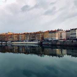 Buildings by river against sky in city