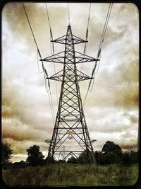 Low angle view of electricity pylon against cloudy sky