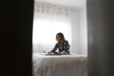 View thru a door ajar of woman having breakfast on bed.