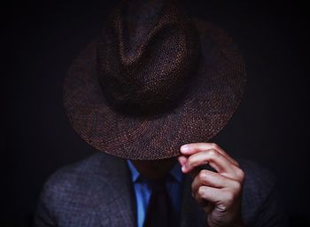 Midsection of person wearing hat against black background