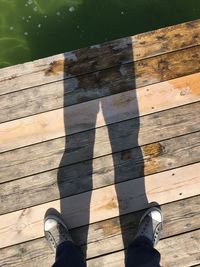 Low section of man standing on wooden pier by lake