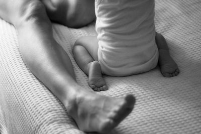 Low section of baby and mother relaxing on bed