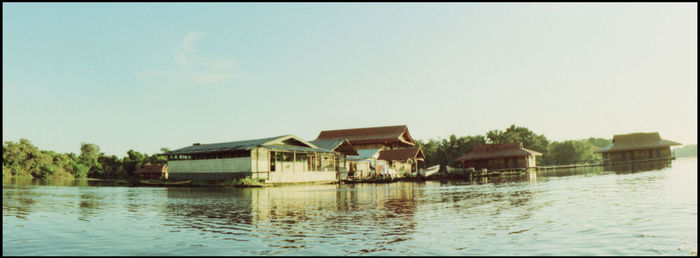 Houses by lake and buildings against clear sky