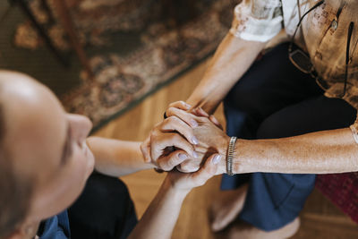 High angle view of senior woman holding hands of female caregiver at home