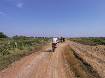 Rear view of man riding motorcycle on dirt road