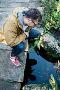 High angle view of man crouching on footpath by pond