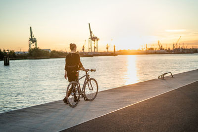 Rear view of person riding bicycle on city during sunset
