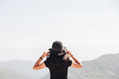 Rear view of woman wearing hat on mountain against clear sky