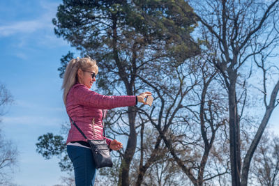 Full side view of an adult woman with sunglasses taking a picture with one hand in a park