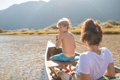 Rear view of woman with son sailing boat in lake against mountains