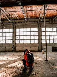 Young man with backpack crouching in abandoned room