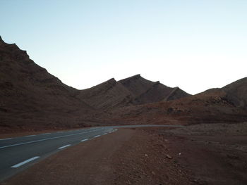 Scenic view of road by mountains against clear sky