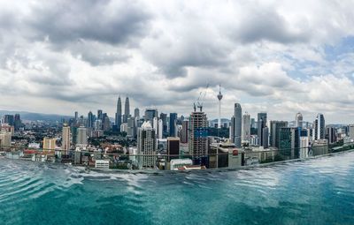 City at waterfront against cloudy sky