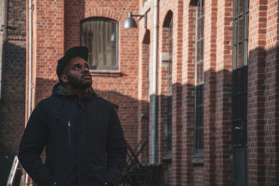 Young man looking away against buildings in city