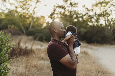 Close up of sweet father kissing newborn girl in backlit field