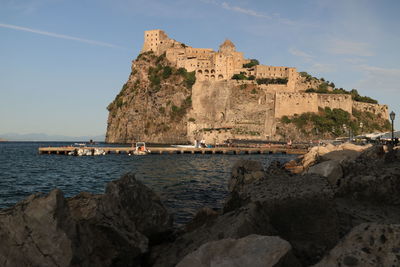 Built structure on rocks by sea against sky