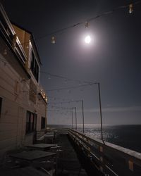 Illuminated street lights by sea against sky at night