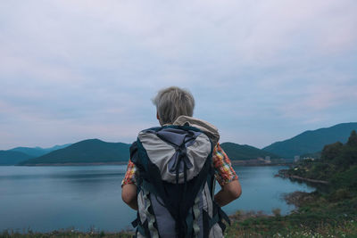 Rear view of backpacker standing at lakeshore against sky