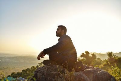 Side view of man sitting on rock during sunset