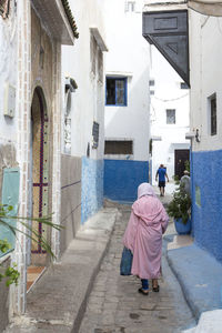 Rear view of people walking on footpath amidst buildings