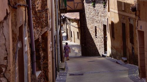 Rear view of man walking on alley amidst buildings in city