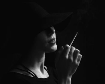 Close-up of woman holding cigarette against black background