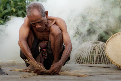 Portrait of shirtless man sitting on wood