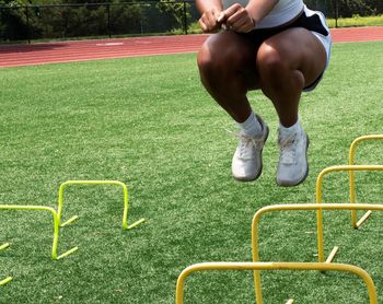 African american female track jumper bounding over two foot high yellow mini hurdles.