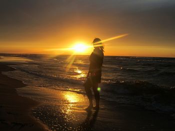 Silhouette woman photographing sea at sunset