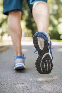 Low section of man in sports shoes running on park street