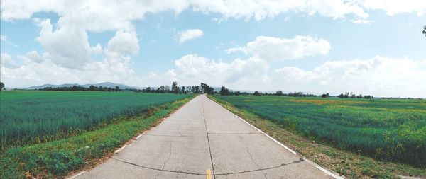 Empty road amidst field against sky