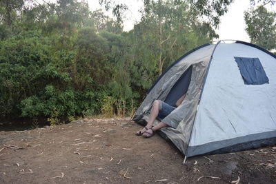 Low section of person sitting on tent in forest
