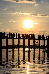 Silhouette people on shore against sky during sunset