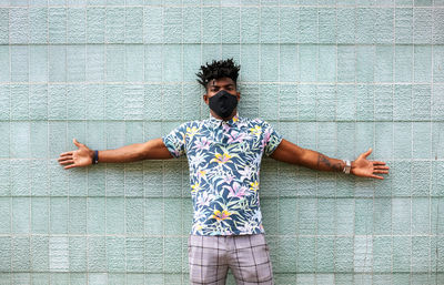 Mid adult man with arms outstretched wearing face mask while standing against wall