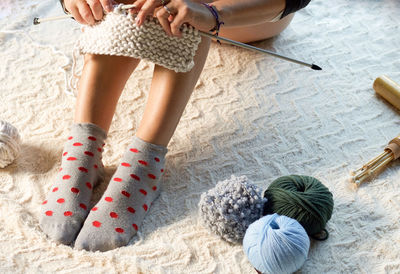 Low section of woman knitting wool while sitting on bed