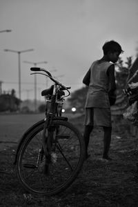 Rear view of boy standing by bicycle on road