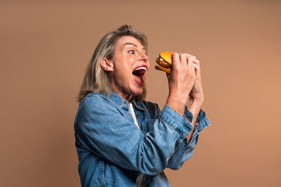 Thoughtful young man talking on phone while standing against yellow background
