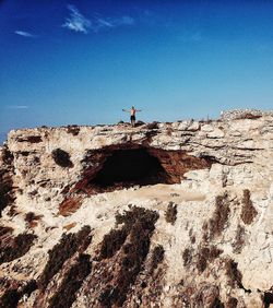 Low angle view of man on rock against blue sky