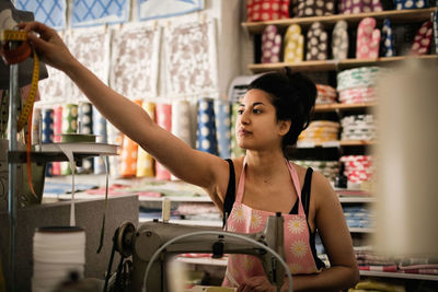 Woman reaching for tape measure while sewing textile in fabric shop